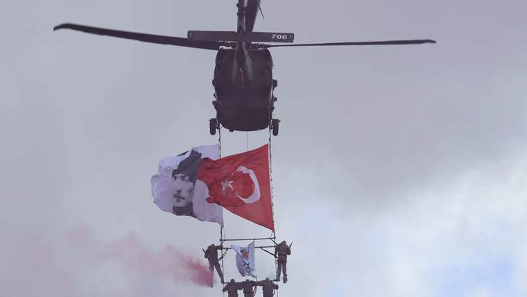 Bir helikopter, aşağıda Türk bayrağı ve Atatürk posteri ile birlikte duman çıkararak uçuyor.