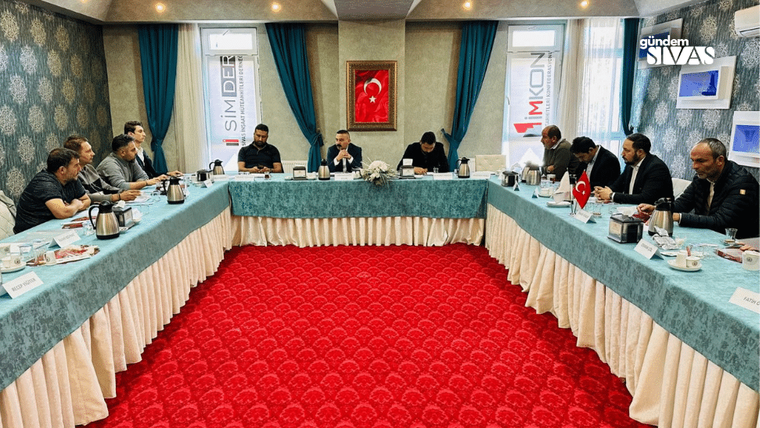 Bir toplantı odasında, uzun bir masa etrafında oturan on bir kişi, masanın üzerinde çaydanlıklar ve Türk bayrağı var.