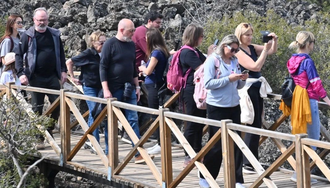 Kayalık alanda ahşap yürüyüş köprüsünden geçen, bazıları fotoğraf çeken bir grup insan görülüyor.
