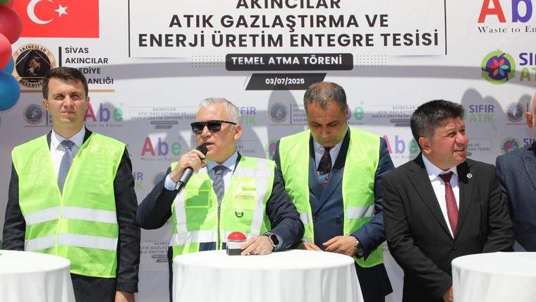 Temel atma töreninde, yeşil yelek giymiş dört kişi bir masanın etrafında konuşuyor.