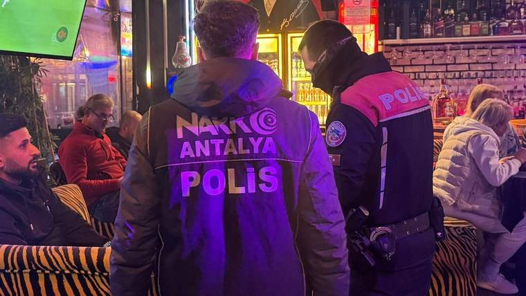 Kapalı bir mekânda, sırtlarında “Narkotik Antalya Polis” yazılı iki polis memuru görülüyor.