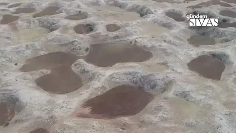Açık renkli, kurak arazide çok sayıda yuvarlak çukur ve bazı çukurlarda koyu renkli yüzeyler görülüyor.