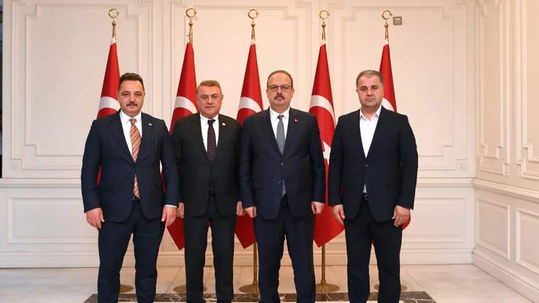 Dört kişi, arka planda Türk bayrakları ile birlikte poz veriyor.