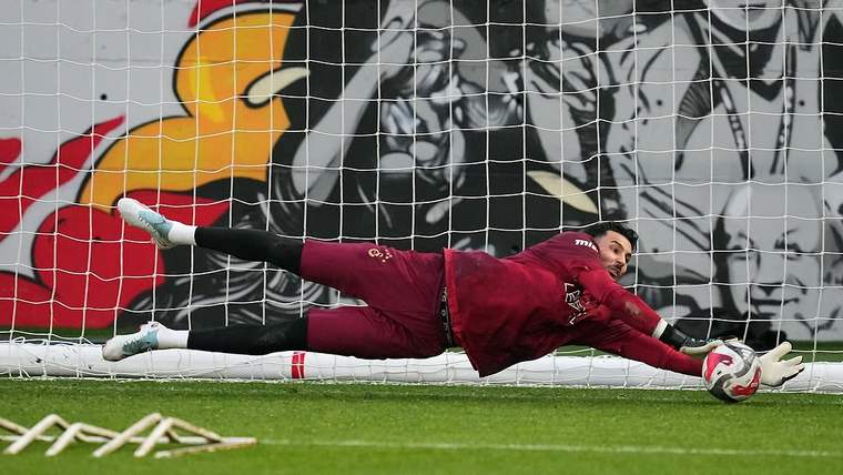 Galatasaray forması giyen kaleci, kale önünde uzanarak topu iki eliyle tutuyor.