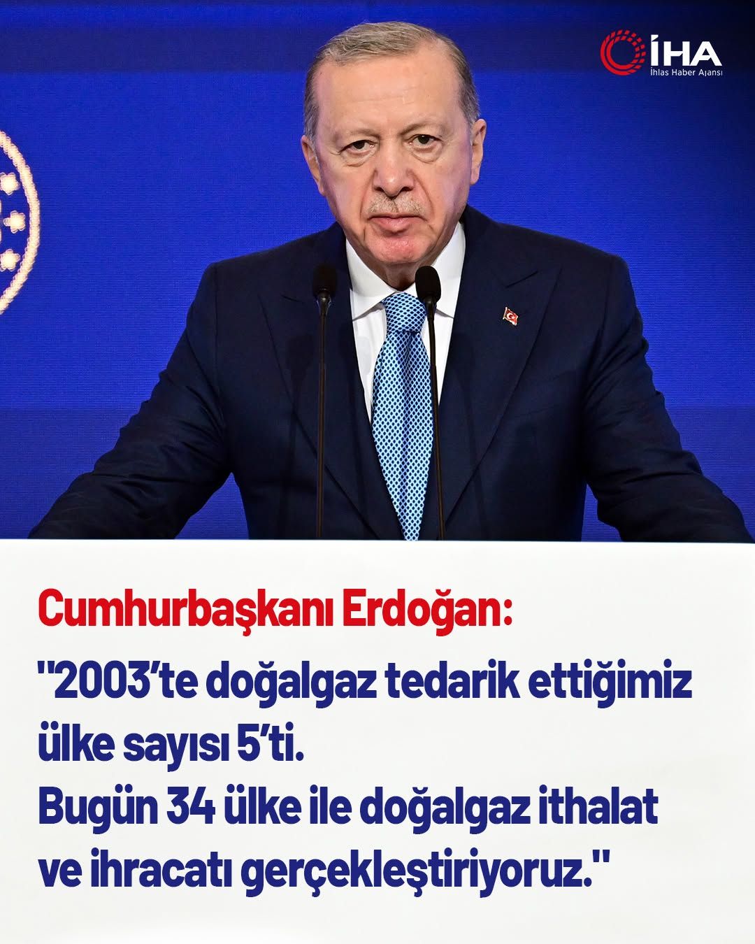 Mavi arka planda mikrofonun önünde konuşan bir kişi, üzerinde Türk bayrağı bulunan bir rozet takıyor.