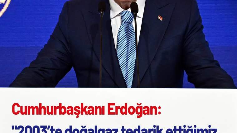 Mavi arka planda mikrofonun önünde konuşan bir kişi, üzerinde Türk bayrağı bulunan bir rozet takıyor.