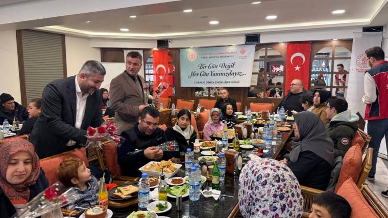 Restoran salonunda çok sayıda kişinin oturduğu masalarda yemekler, içecekler ve çiçek buketi görülüyor.