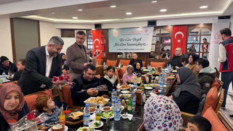 Restoran salonunda çok sayıda kişinin oturduğu masalarda yemekler, içecekler ve çiçek buketi görülüyor.
