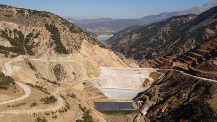 Dağlık vadide, kuru yamaçlar arasında beton gövdesi ve az miktarda su görünen bir gölet bulunuyor.