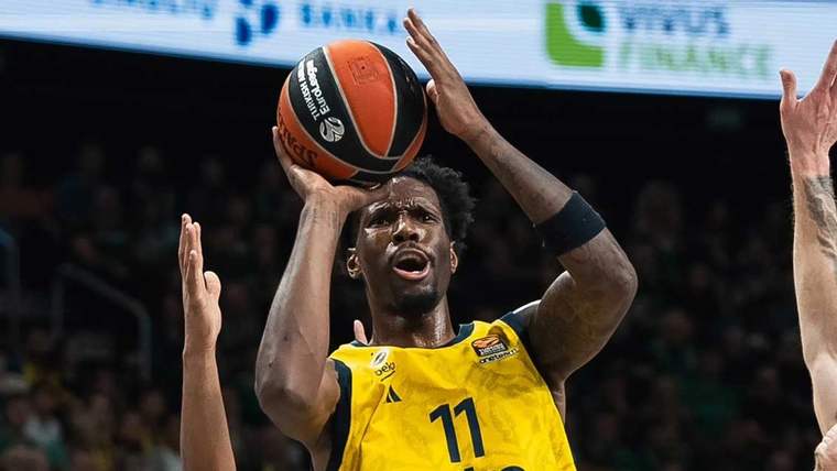 Sarı-lacivertli forma giymiş bir basketbolcu, topu potaya atmaya hazırlanıyor.