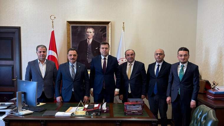 Masa arkasında takım elbiseli altı kişi, Türk bayrağı ve duvardaki portre önünde yan yana duruyor.