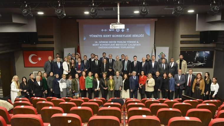 Bir toplantı salonunda, katılımcılar grup halinde poz veriyor; arka planda Türkiye bayrağı ve bir pankart var.