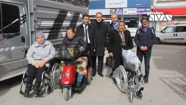 Kaldırımda iki tekerlekli sandalye kullanan kadın ve yanlarında duran beş kişi birlikte görülüyor.