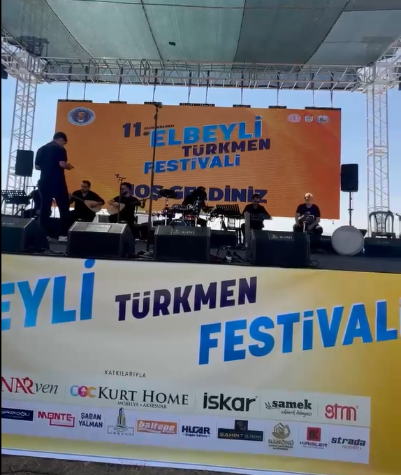 Sahne üzerinde müzisyenler, arka planda festival afişi ve pankartlar yer alıyor.