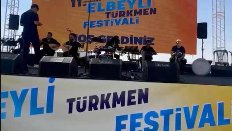 Sahne üzerinde müzisyenler, arka planda festival afişi ve pankartlar yer alıyor.