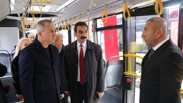 Bir otobüsün içinde üç erkek ve iki kadın, ön bölümde ayakta durarak konuşuyor.