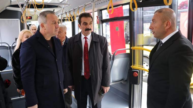 Bir otobüsün içinde üç erkek ve iki kadın, ön bölümde ayakta durarak konuşuyor.