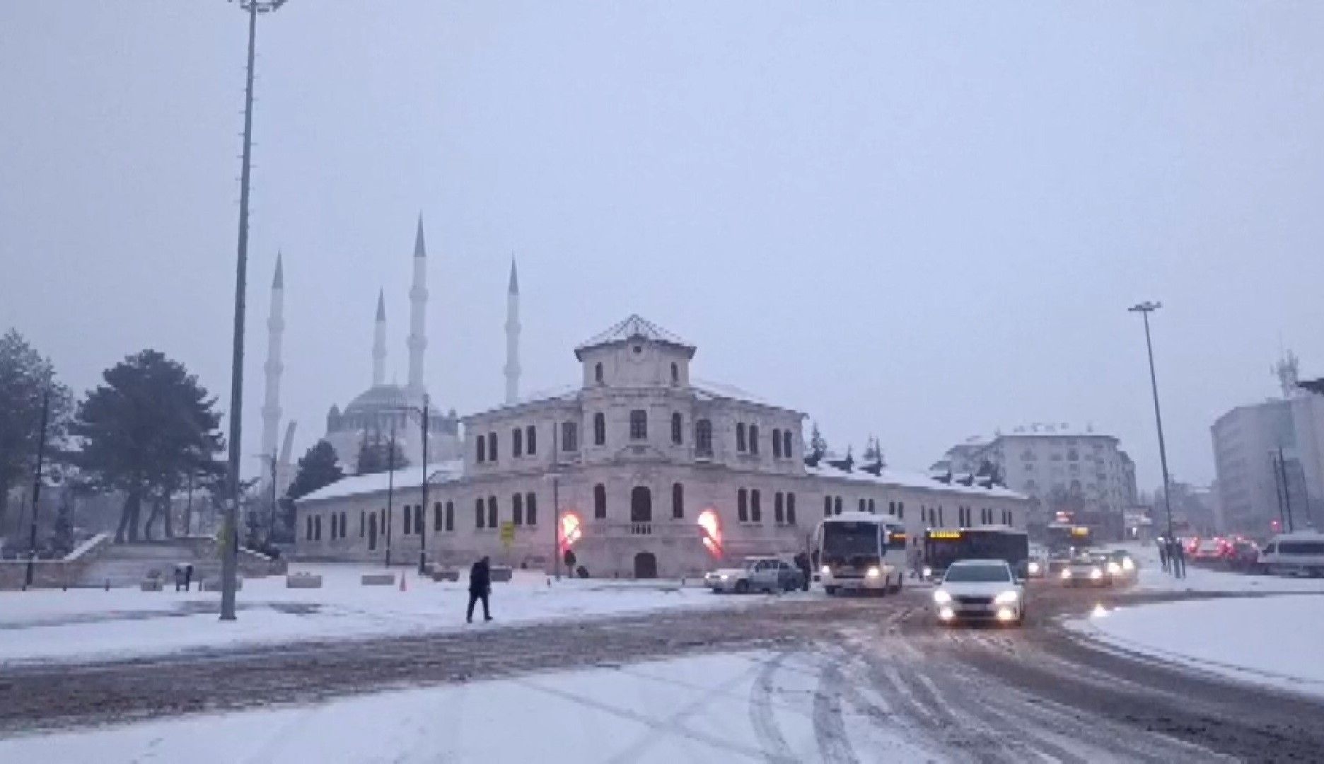 Karla kaplı bir cadde üzerinde, tarihi bir bina ve cami görünmektedir.