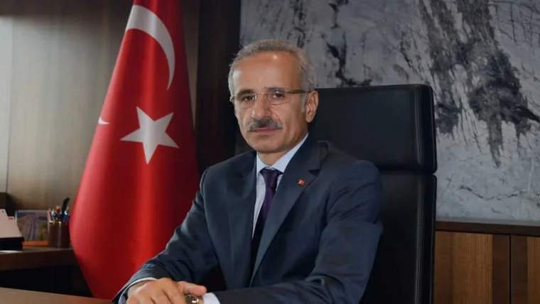Kürsüde oturan bir kişi, arkasında Türk bayrağı var.