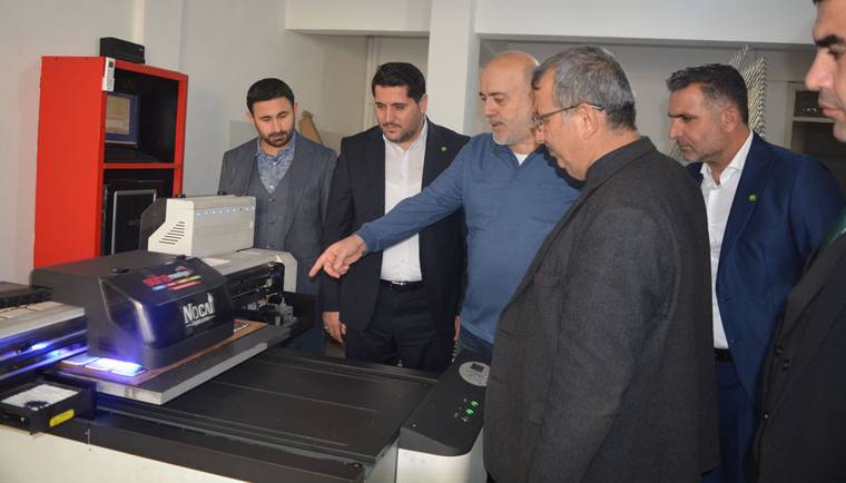Bir grup erkek, bir makineyi inceliyor; biri makineye işaret ediyor.