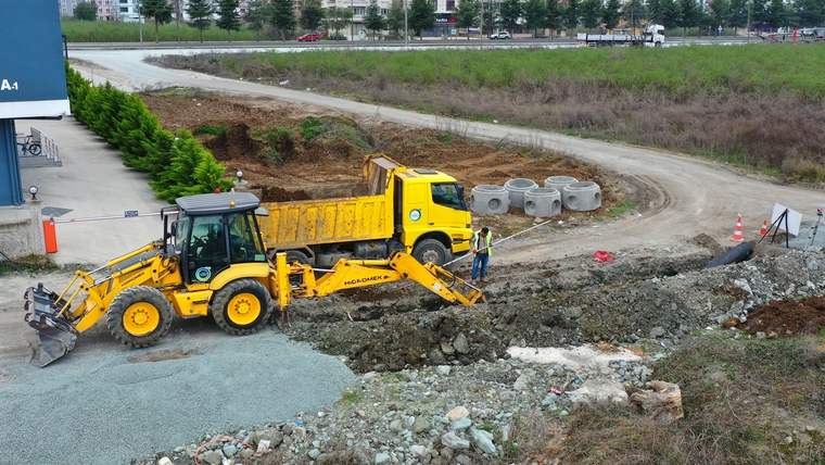 Sarı bir kazıcı yükleyici, toprak alanda açılmış çukurun yanında çalışırken görülüyor; beton halkalar ileride duruyor.