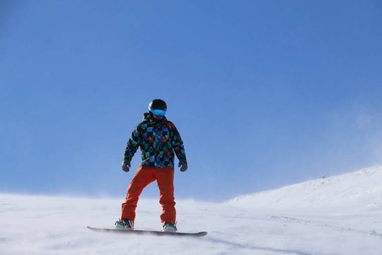 Karlı bir yamaçta, renkli mont ve kırmızı pantolon giyen kişi snowboard üzerinde duruyor.