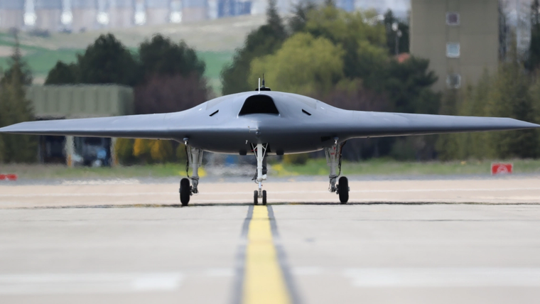 Kanatları geniş, pilotsuz hava aracı pistte sarı çizgi üzerinde önden görünümüyle duruyor.
