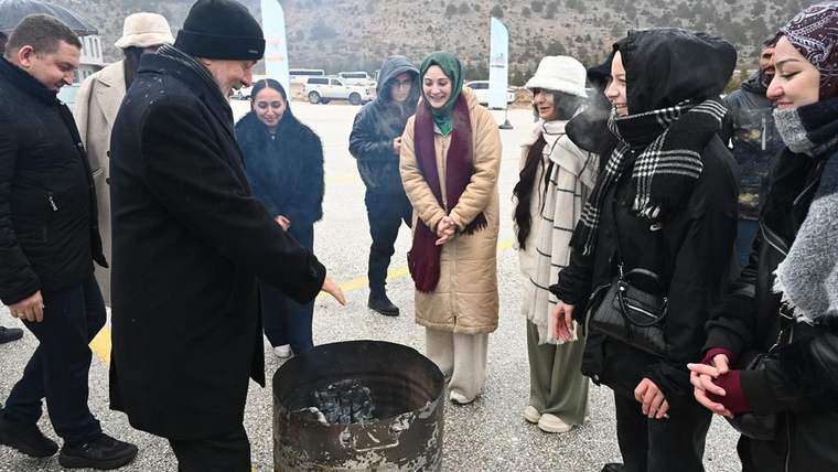 Dağlık alanda bir grup insan, içinde köz bulunan metal bir kabın çevresinde duruyor.