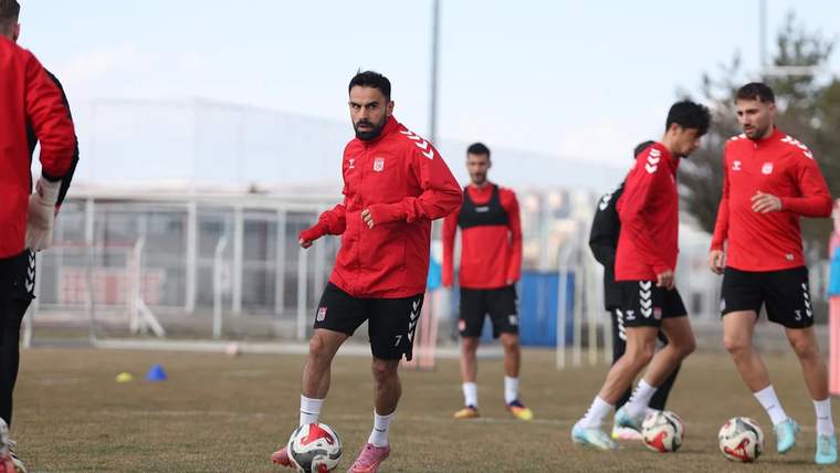 Antrenman yapan futbolcular, kırmızı formalar giymiş, sahada koşuyorlar.