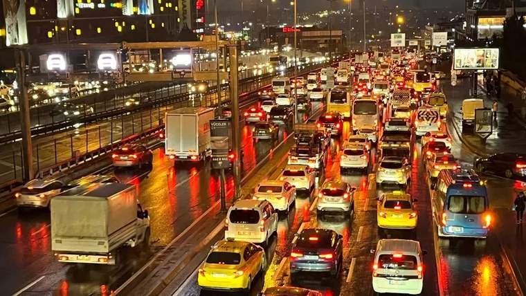 Gece saatlerinde yoğun bir trafik, ıslak yolda ilerleyen araçlar ve ışıklar yansıyor.