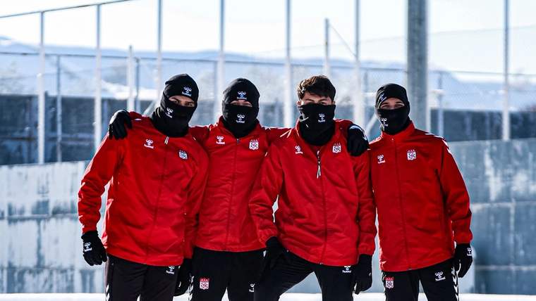 Kırmızı mont giymiş dört futbolcu, karlı bir alanda poz veriyor.