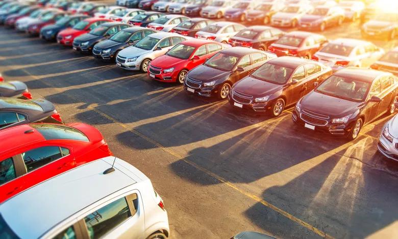 Güneş ışığı altında, otoparkta sıralanmış farklı renk ve modellerde çok sayıda otomobil görülüyor.