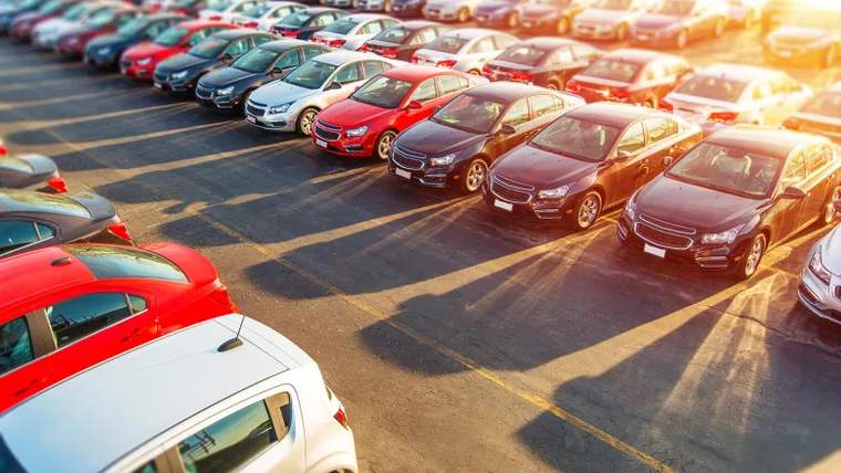 Güneş ışığı altında, otoparkta sıralanmış farklı renk ve modellerde çok sayıda otomobil görülüyor.