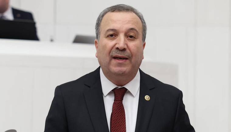 Kürsüde konuşan bir kişi, resmi bir kıyafet giymekte ve mikrofon kullanmaktadır.