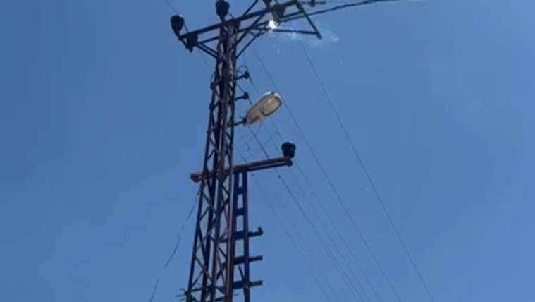 Metal elektrik direğinde çok sayıda izolatör ve havai hat kabloları, direğe bağlı sokak lambasıyla birlikte görülüyor.