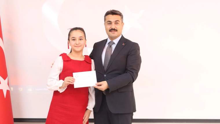 Kırmızı elbise giymiş bir öğrenci, elinde belge tutarak bir erkeğe gülümsüyor.