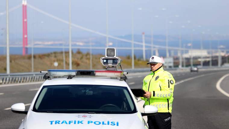 Üzerinde “Trafik Polisi” yazan araçta kamera düzeneği ve yanında reflektif giysili bir polis memuru görülüyor.
