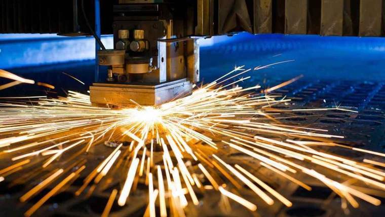 Metal levhayı kesen endüstriyel makinenin ucundan çevreye parlak kıvılcımlar saçılıyor.