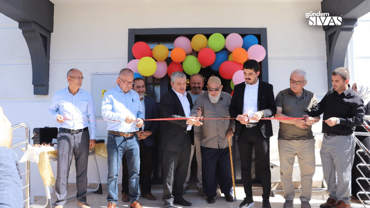 Renkli balonlarla süslenmiş bir kapının önünde, kurdele kesen bir grup erkek.