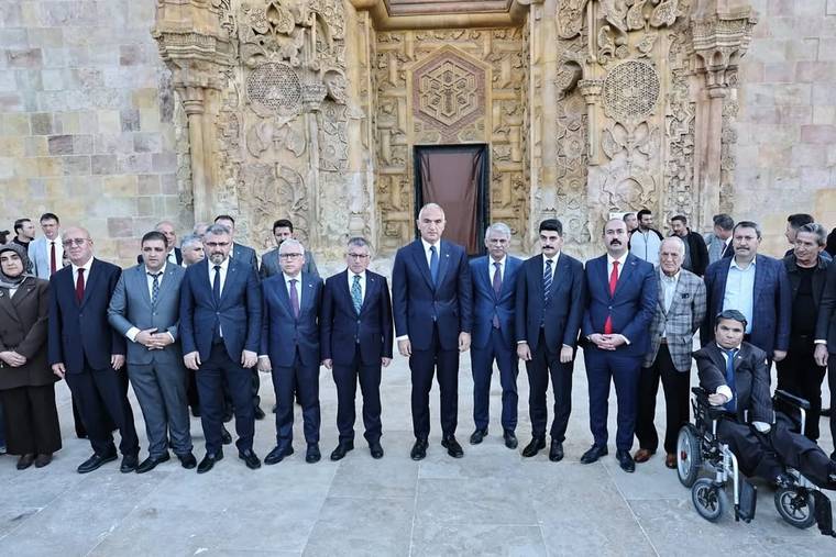 Süslemeli taş kapı önünde, aralarında tekerlekli sandalye kullanan bir kişinin bulunduğu kalabalık grup duruyor.