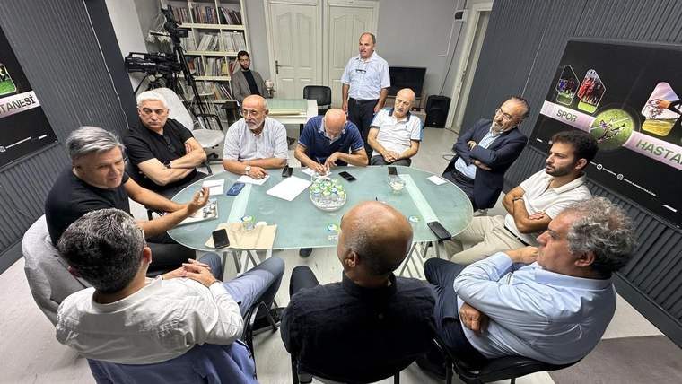 Bir grup erkek, yuvarlak bir masanın etrafında toplanmış, tartışma yapıyor.