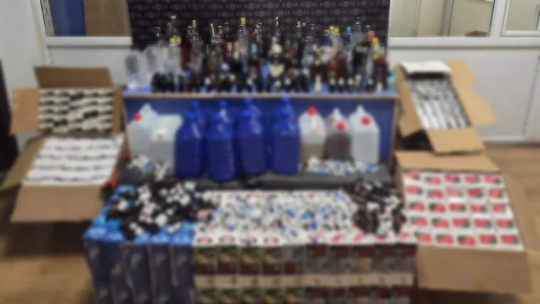Çeşitli alkol şişeleri ve kutuları, mavi bidonlar ve ambalajlar bir masanın üzerinde yer alıyor.