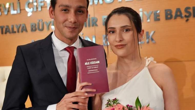 Takım elbiseli bir erkek ve beyaz elbiseli bir kadın, aile cüzdanı ve çiçek buketi tutuyor.