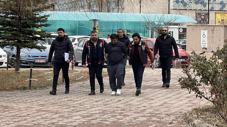 Gözaltındaki bir kişi, polis eşliğinde yürüyerek bir alandan geçiyor.