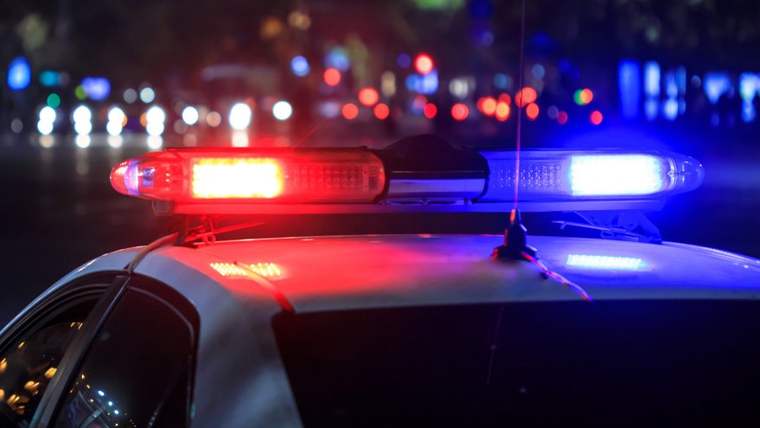 Mavi ve kırmızı ışıklar yakan bir polis aracı, karanlık bir sokakta duruyor.