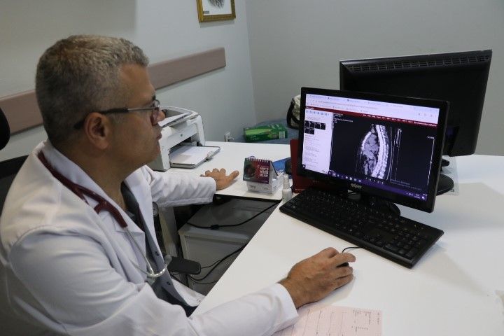 Beyaz önlük giymiş bir doktor, bilgisayar ekranında bir görüntü inceliyor.