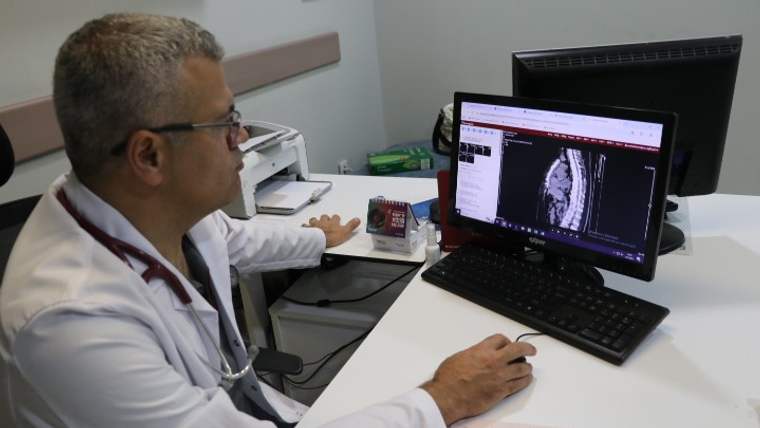 Beyaz önlük giymiş bir doktor, bilgisayar ekranında bir görüntü inceliyor.