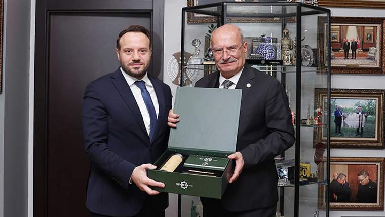 İki erkek, açık bir kutu içindeki belgeyi tutarak sergileme dolaplarının önünde poz veriyor.