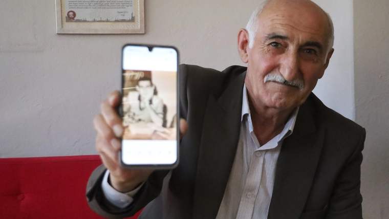 Bir adam, elindeki akıllı telefonun ekranında eski bir fotoğrafı gösteriyor.