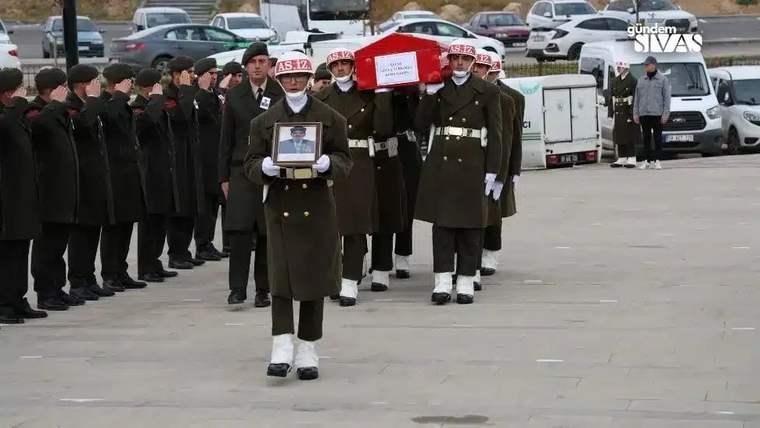 Üniformalı askerler, üzerinde Türk bayrağı bulunan kırmızı örtülü bir tabut ve çerçeveli fotoğraf taşıyor.